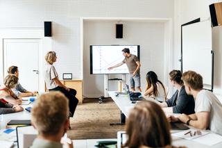 A student giving a presentation to the class during a seminar session and using a large monitor as a visual aid.